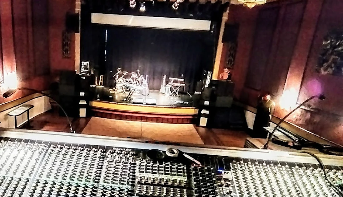 A theater stage with the band's instruments, seen from the mixing console